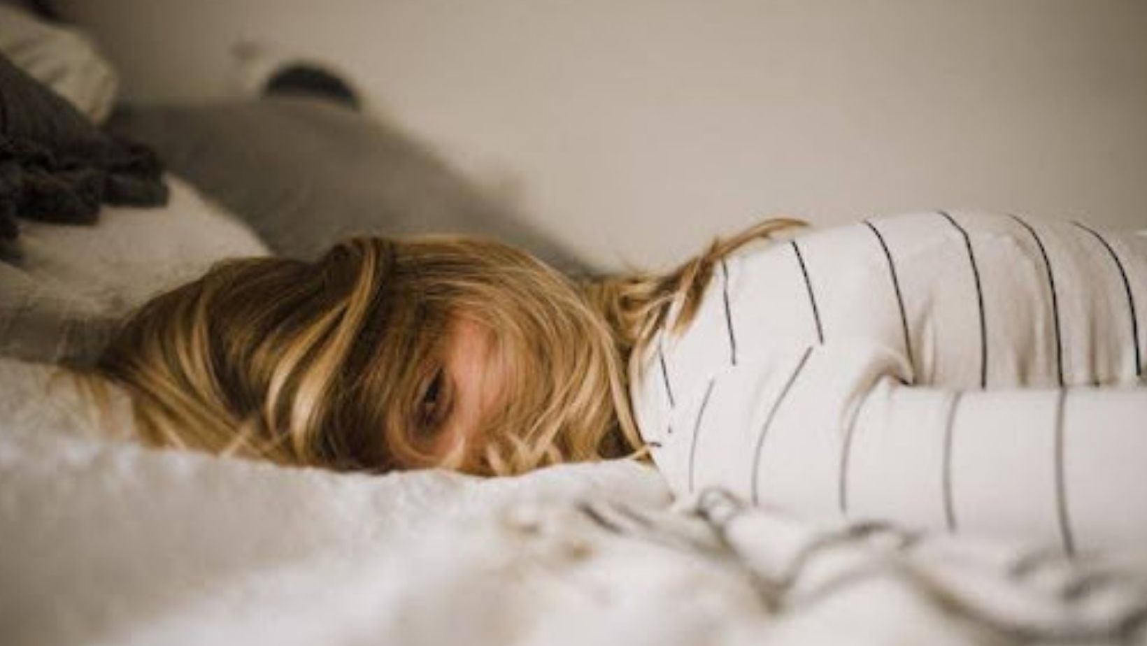 A blonde woman in a striped shirt lying face down on a bed.